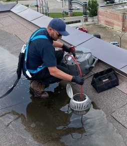 plumber works to unplug roof drain with auger